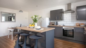 A modern kitchen with a central island, bar stools, a refrigerator, oven, and a microwave.