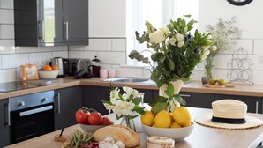 A kitchen counter with fresh vegetables, fruits, and a cheese wheel.