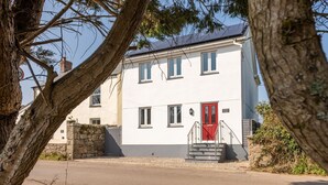 A two-story house with a red door and a stone wall.