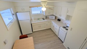 Una cucina compatta con mobili bianchi, un frigorifero, un forno a microonde, un piano cottura e una ventola a soffitto.