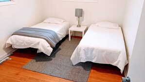 Una stanza piccola e pulita con due letti singoli, un comodino con lampada e un tappeto sul pavimento in legno.