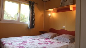 Quarto com cama, janela com cortinas, mesa de cabeceira e prateleira na parede com uma luminária.