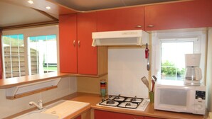 Cozinha compacta com pia, fogão, micro-ondas e armários vermelhos.