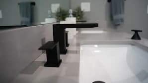 Een moderne badkamer met een grote spiegel, een zwarte wastafel en een wit aanrecht.