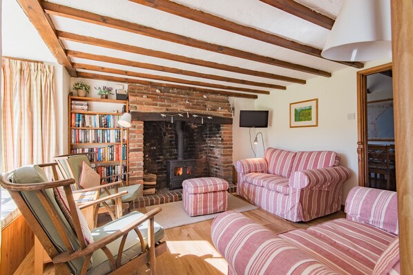 A cozy living room with a brick fireplace, striped sofas, a bookshelf, and wooden beams on the ceiling. - The Nest by Bloom Stays - seaside cottage sleeping 6 guests in 3 bedrooms (Romney Marsh)