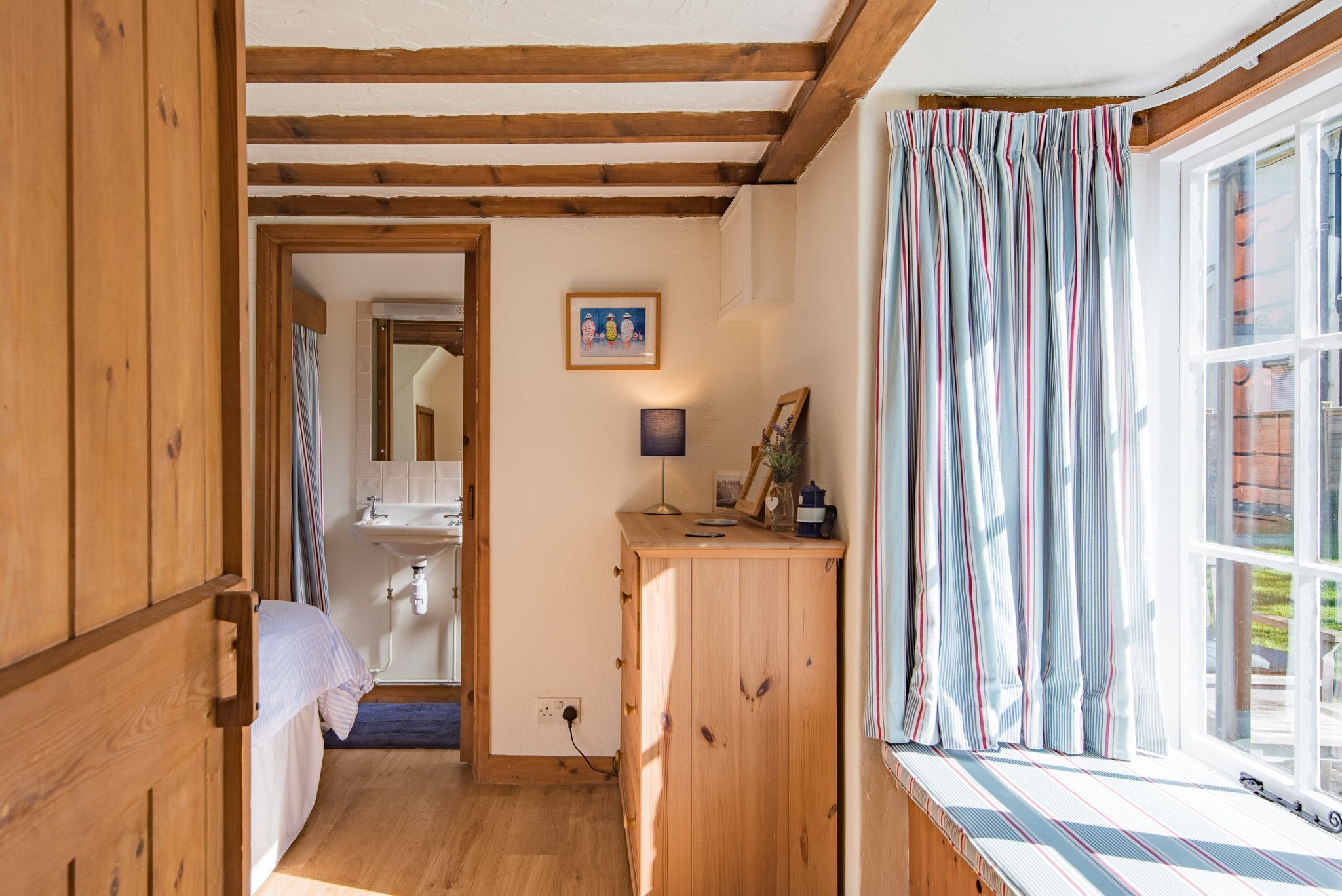 Een kamer met houten vloer, een raam, nachtkastje en een bed.