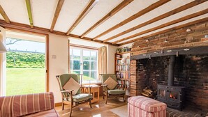 Una sala de estar acogedora con chimenea, vigas de madera, una estantería y vistas al exterior.