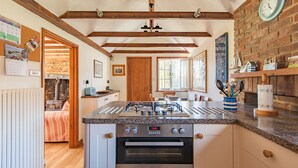 Una cocina con una isla central, vigas de madera, pared de ladrillo y un reloj.
