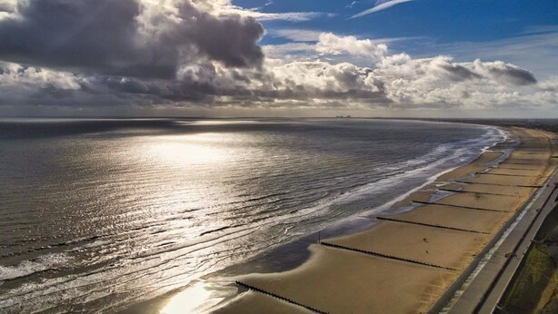 Una playa con una extensa orilla arenosa, cielo despejado y mar tranquilo.