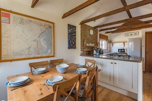 A dining table set with plates and cutlery, a map on the wall, and a kitchen area with appliances. - The Nest by Bloom Stays - seaside cottage sleeping 6 guests in 3 bedrooms (Romney Marsh)