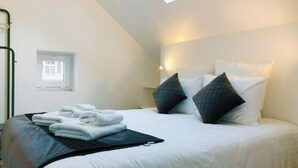 A neatly made bed with white linens and two dark pillows, a small window with a calendar, and a skylight above. - App*** 2/3 pers "Nuage" ☁️ Air-conditioned with garden (Lons-le-Saunier)