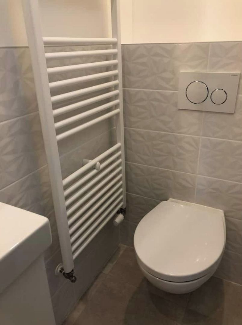 Un baño con un radiador blanco, un inodoro y un interruptor de luz en la pared.