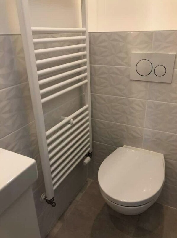 A bathroom with a white radiator, a toilet, and a wall-mounted light switch.