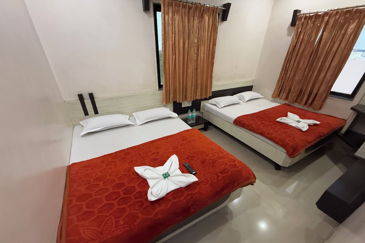 A hotel room with two beds, each with a red bedspread and white pillows. There are two bottles of water on the nightstand, and a window with curtains.