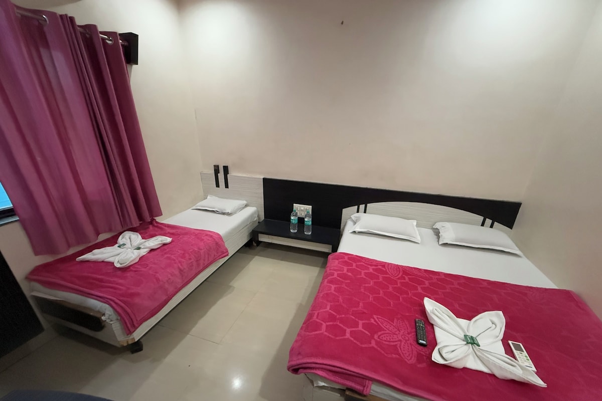 A hotel room with two beds, each with a pink bedspread and white pillows. There is a small table between the beds with a bottle of water and a tissue box.