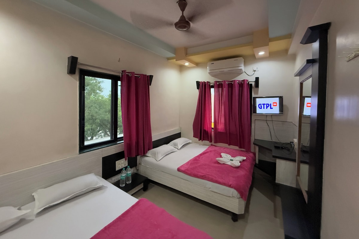 A hotel room with two beds, a ceiling fan, an air conditioning unit, a TV, and a window with curtains.