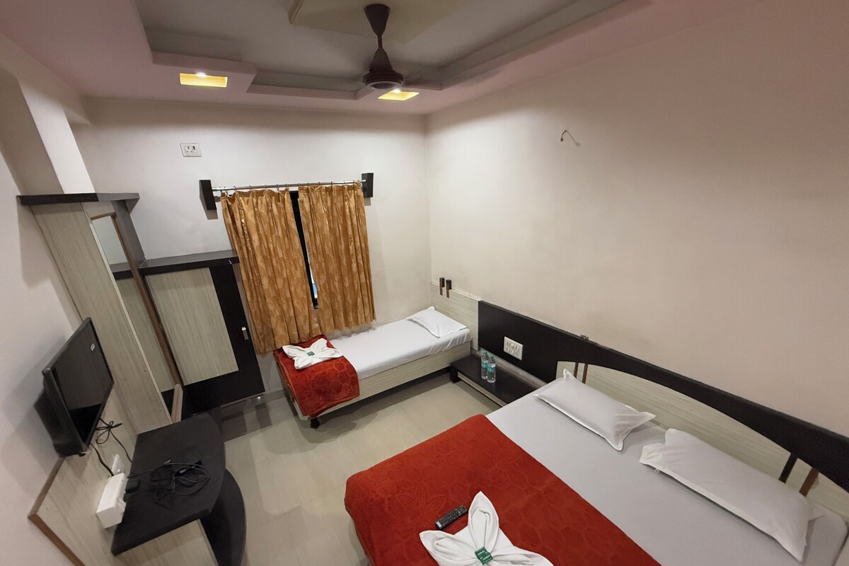A hotel room with two single beds, a desk with a chair, a TV, and a wardrobe.