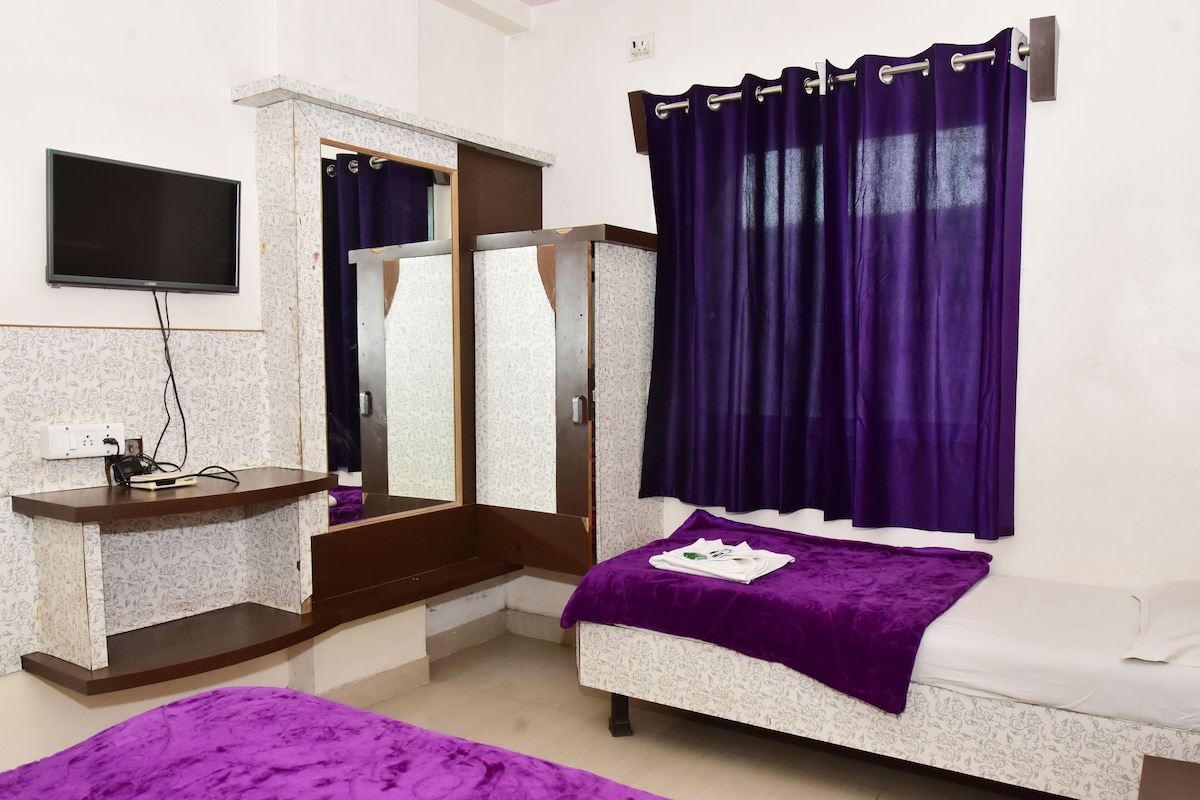 A bedroom with a bed, a vanity with a mirror, a television, and purple curtains.