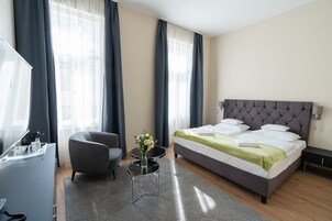 A modern hotel room with a bed, a desk, a chair, and a small table with a vase of flowers.