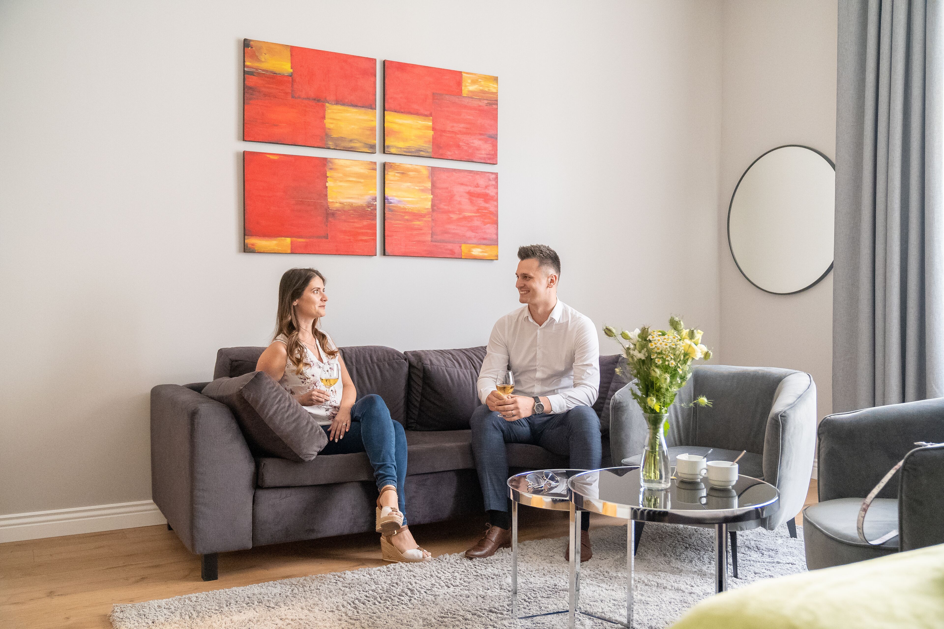 A modern living room with a grey sofa, a coffee table, and a vase with flowers.