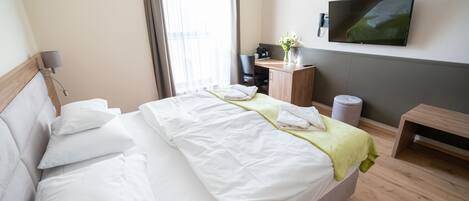 A hotel room with a bed, a desk, a chair, a TV, and a window with curtains.