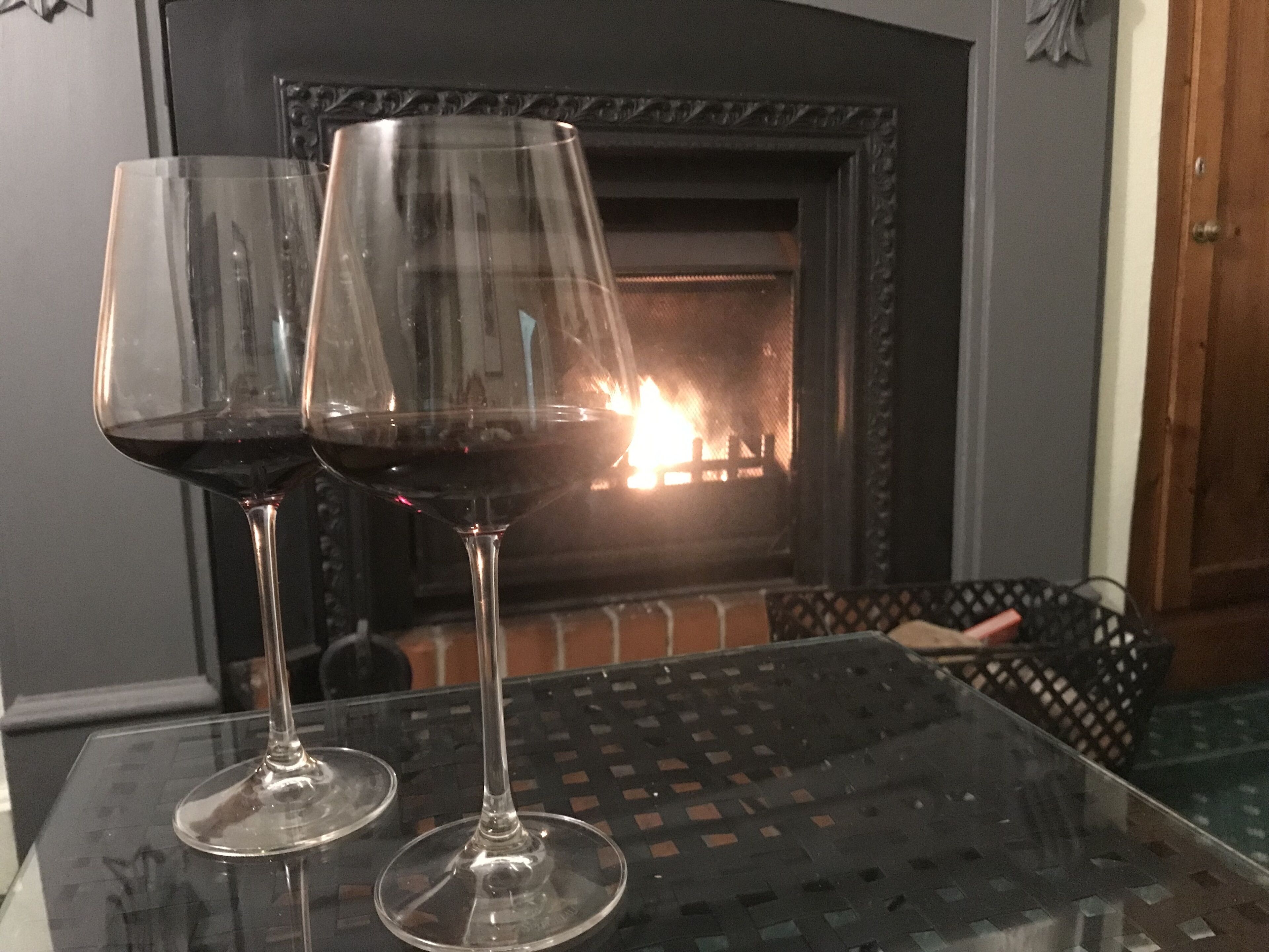 Two wine glasses on a glass table with a fireplace in the background.