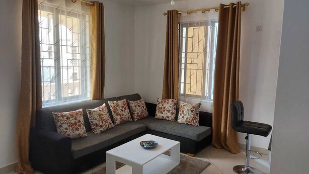 Ein modernes Wohnzimmer mit einem grauen Ecksofa, floralen Kissen, einem weißen Couchtisch und einem schwarzen Sessel.