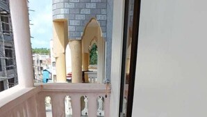 Ein Balkon mit Fliesenboden, einer pinkfarbenen Brüstung und Blick auf ein Gebäude mit Ziegelaußenwand.