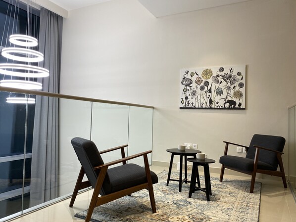 A modern living room with a glass balustrade, two dark armchairs, a small coffee table, and a patterned rug.