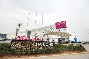A modern AEON Mall with a distinctive architectural design, featuring a large AEON sign and a stone wall entrance.