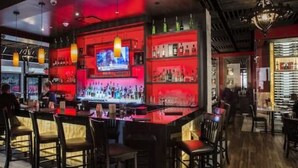 Eine Bar mit einer langen Theke, verschiedenen Sitzmöglichkeiten und einem Fernsehbildschirm.