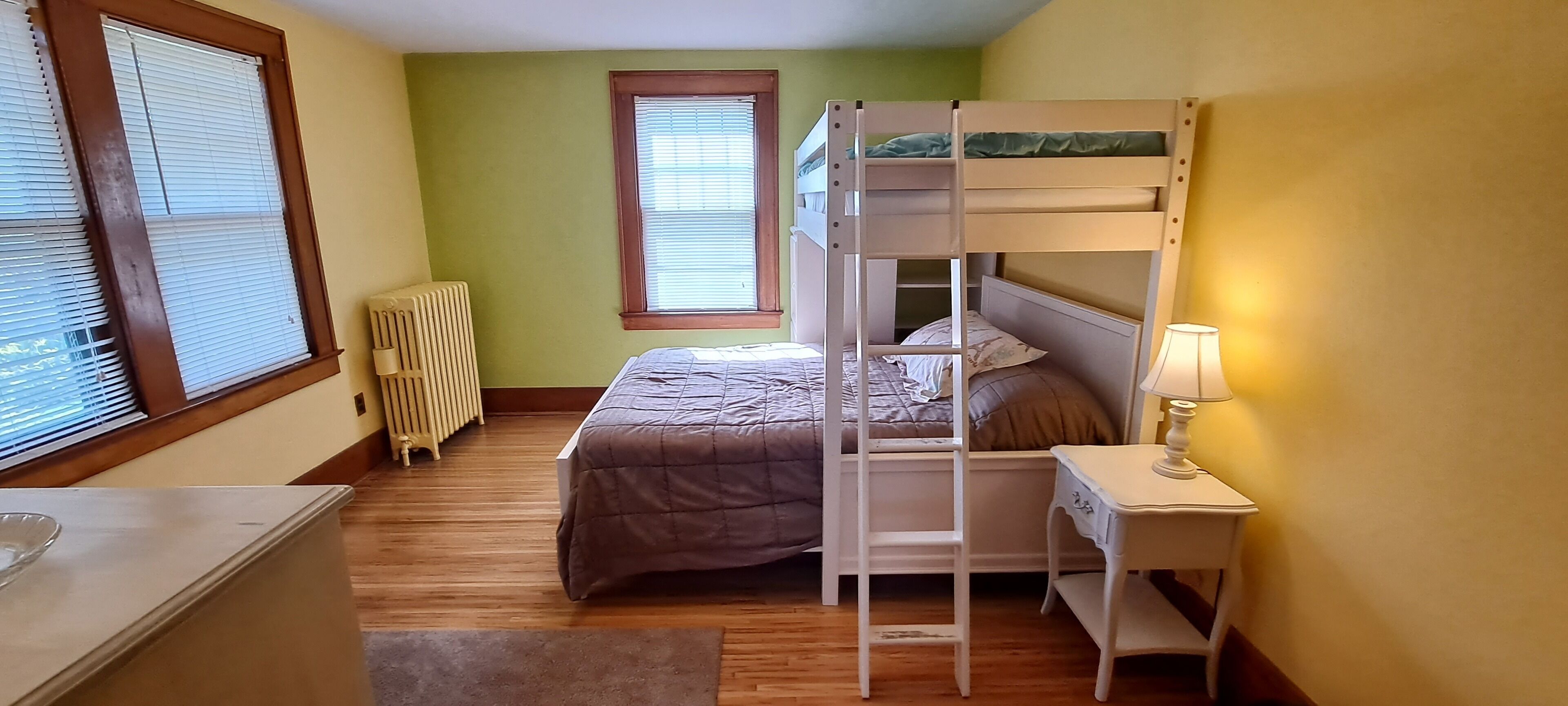 A bunk bed room with a window, radiator, bedside table, and lamp.
