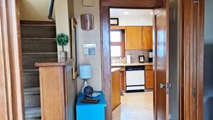 Ein Flur, der zu einer Küche mit Holzausstattung, einem blauen Schrank und einer Treppe führt.