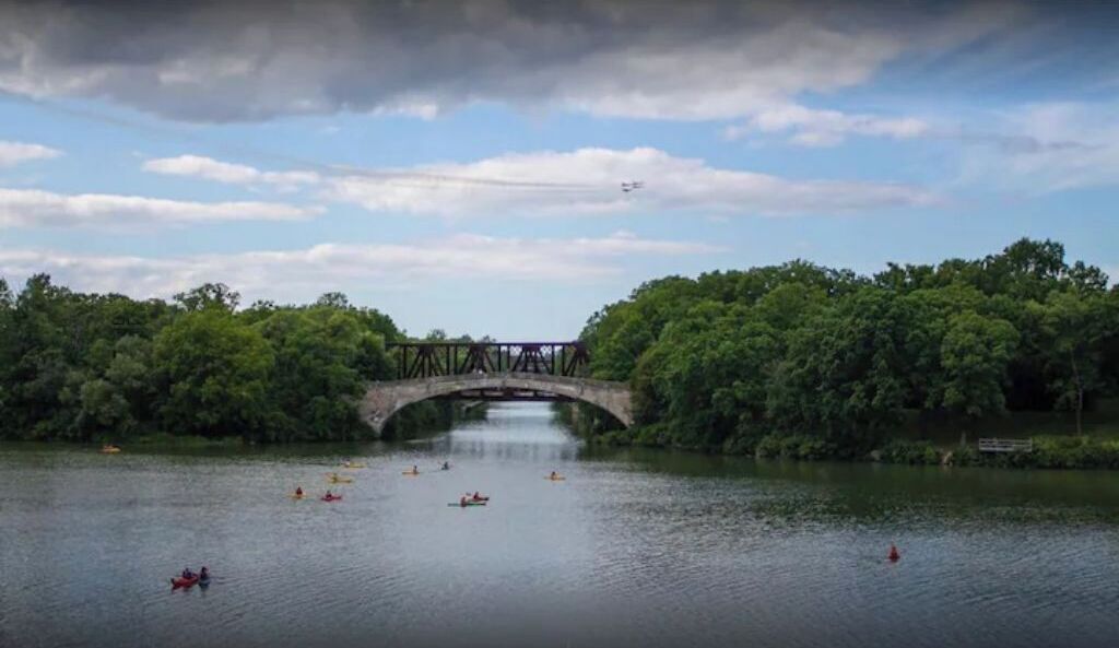 A stone bridge over a calm river with kayaks on the water.