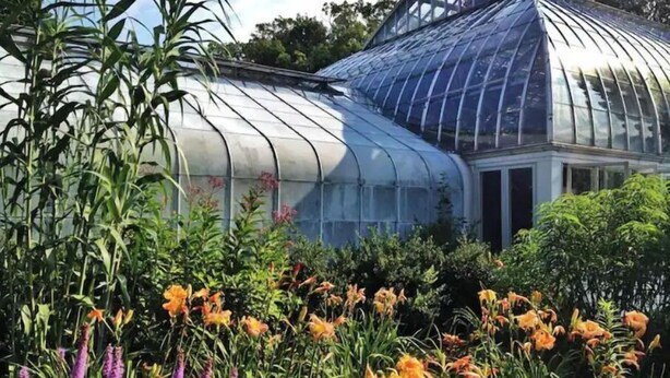 Ein Gewächshaus mit einer gewölbten Glasdecke, umgeben von verschiedenen Pflanzen und Blumen.