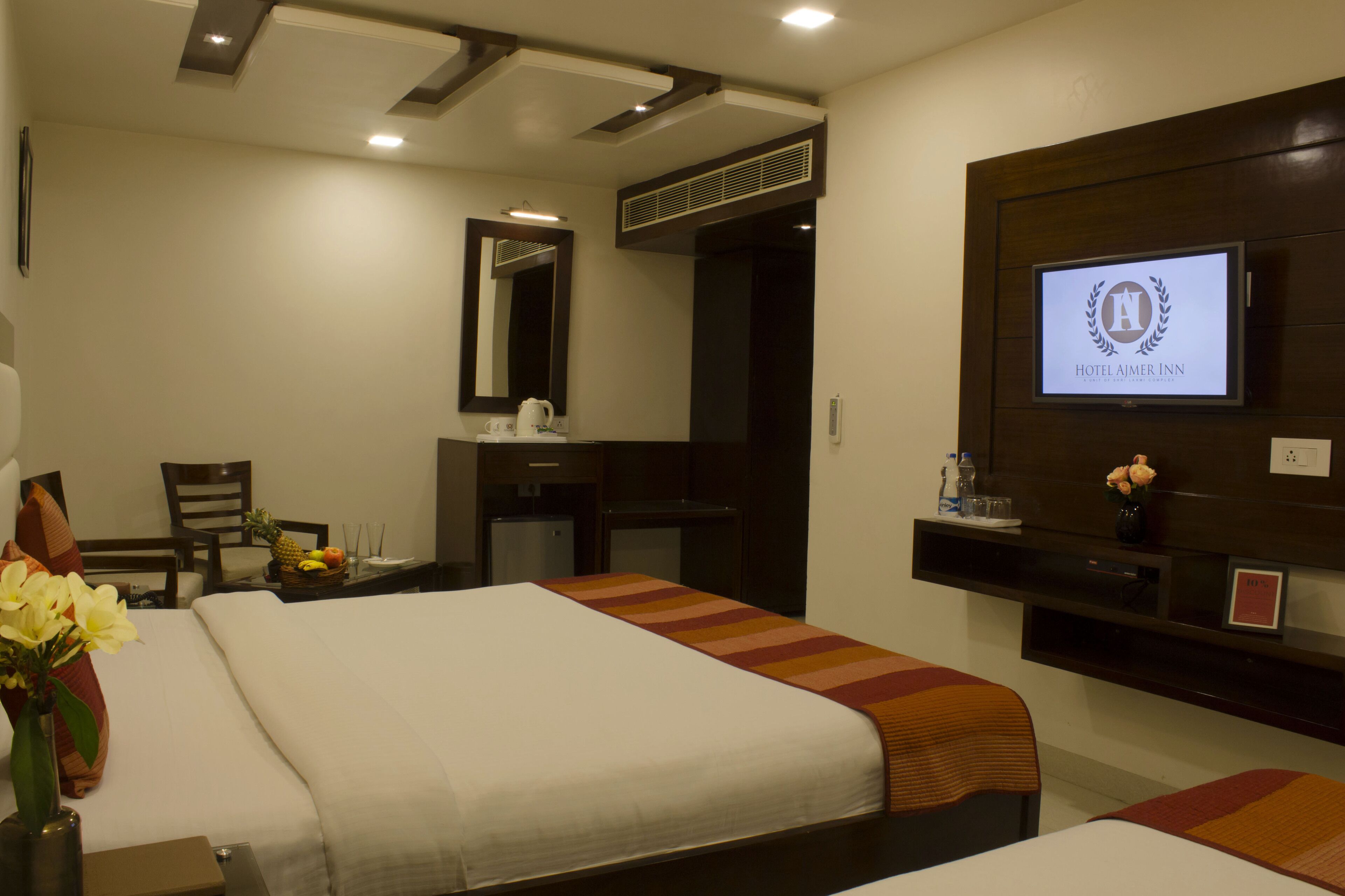 Una habitación de hotel con cama, escritorio, silla, televisor y espejo.