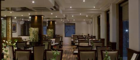 A hotel dining area with multiple tables set for guests, chairs, and decorative plants.