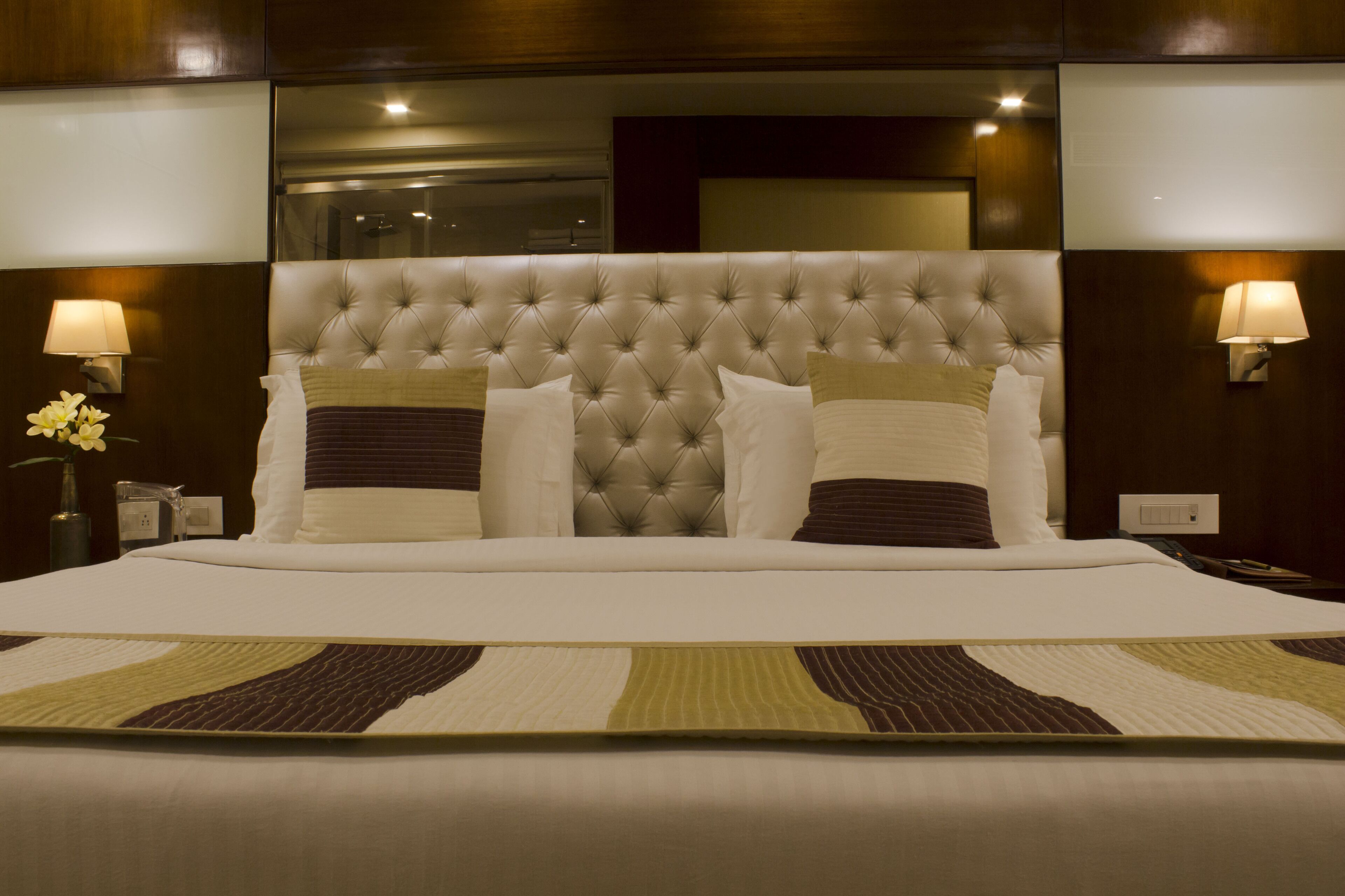 Una cama grande con cabecera capitonada, dos lámparas de noche y una mesita de noche decorativa con un florero.