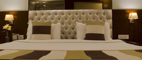 Una cama grande con cabecera capitonada, dos lámparas de noche y una mesita de noche decorativa con un florero.