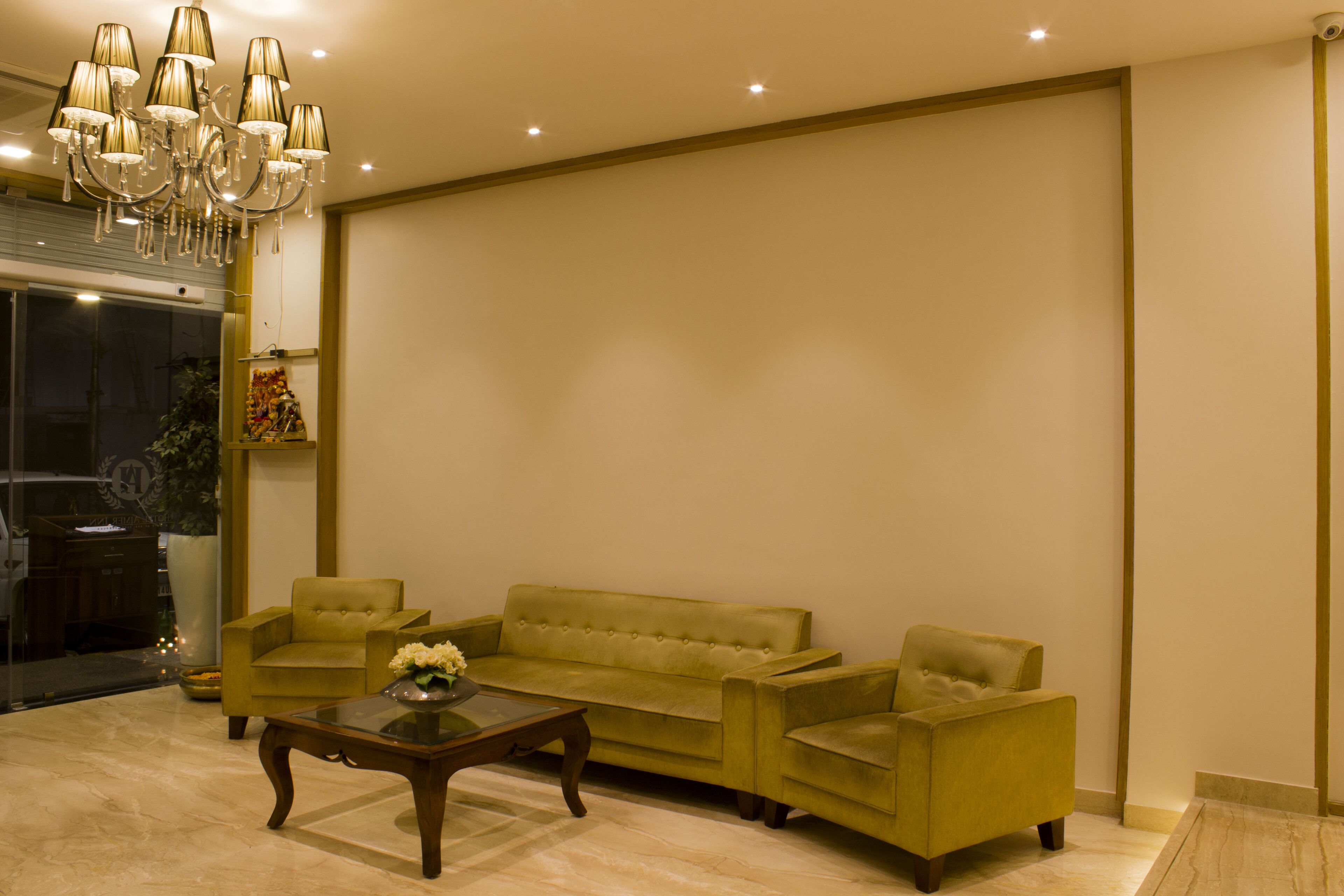 A spacious living room with a green sofa set, a wooden coffee table, and a chandelier.