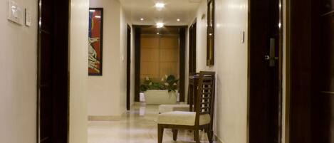 A hallway with a marble floor, wooden doors, and a chair in the distance.