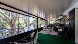 Quarto com uma janela grande com vista para a água, uma cadeira suspensa e uma área de estar com mesa e cadeiras.