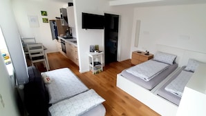 A compact, well-lit room with a kitchenette, two beds with matching bedding, a small table, and a TV mounted on the wall. - Guesthouse Buberl, near Legoland and Skylinepark (Krumbach (Schwaben))