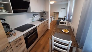 A compact kitchen with a stove, oven, and sink. There is a dining area with a table and a chair. - Guesthouse Buberl, near Legoland and Skylinepark (Krumbach (Schwaben))