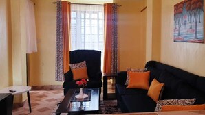 A living room with a black sofa, a black armchair, and a coffee table with a vase of flowers. - Stay.Plus TRM Apartments (Nairobi)