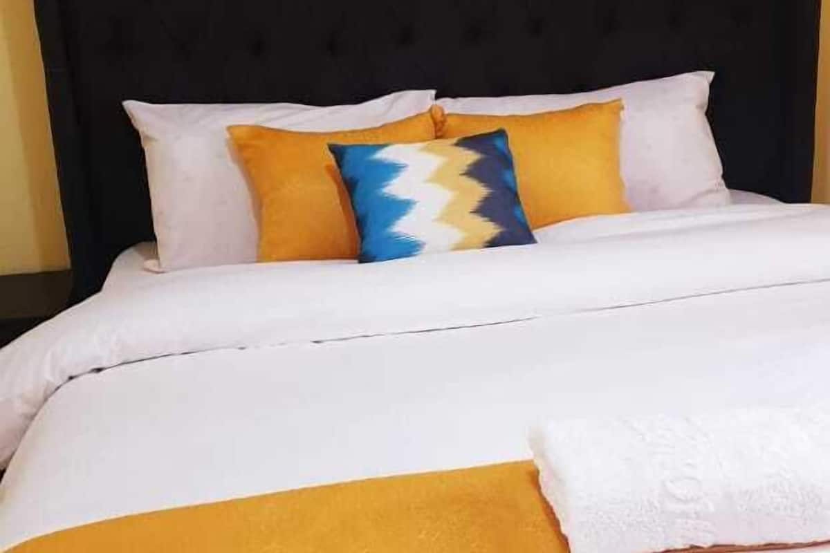 A bed with a black headboard, white bedding, and multiple pillows in various colors.