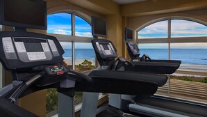 Ein Fitnessraum mit Laufbändern und Trainingsgeräten, große Fenster mit Meerblick.