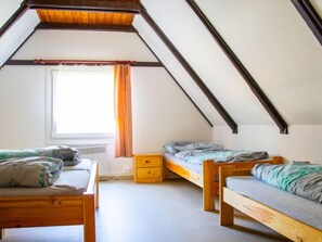 Ein Schlafsaalzimmer mit zwei Holzbettgestellen, einem kleinen Nachttisch und einem Fenster mit Vorhängen.