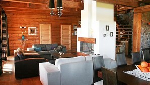 Interior de una cabaña de troncos con chimenea, vigas de madera y un rincón de estar acogedor.