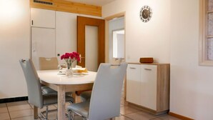A dining area with a round table, four chairs, a vase with flowers, and a cabinet with a mirror. - Vacation home Terry by Interhome (Olivone)